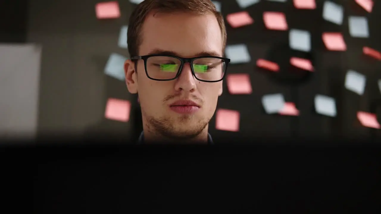 Young Smiling Man In Glasses Working At A Laptop In The Office