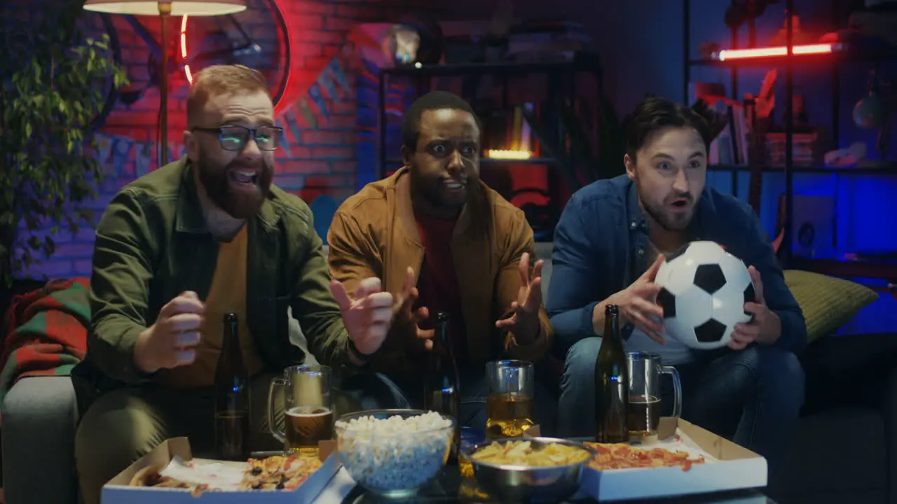 Three Mixed Races Young Male Sport Fans Watching Football On Tv In The Evening In The Dark Living Room The Celebrating Victory Cheerfully