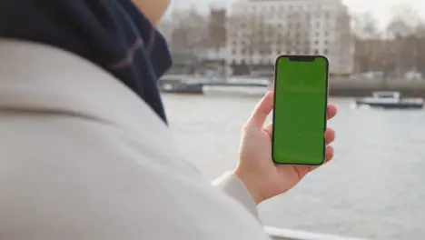 Close Up Of Man Holding Green Screen Mobile Phone Looking Out To River Thames And Embankment In London UK 1