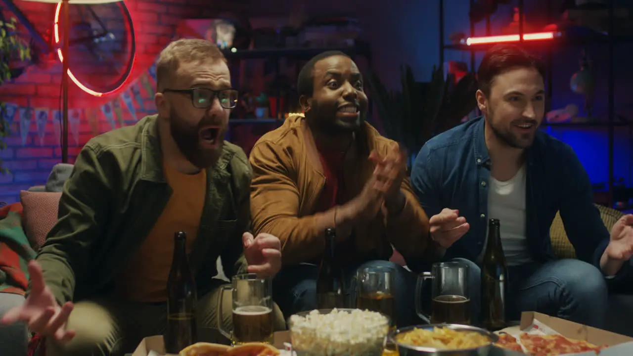 Three Mixed Races Male Friends Resting In The Evening At Home With Beer And Cheering Up For A Goal On The Couch In Front Of Tv With Sport Channel