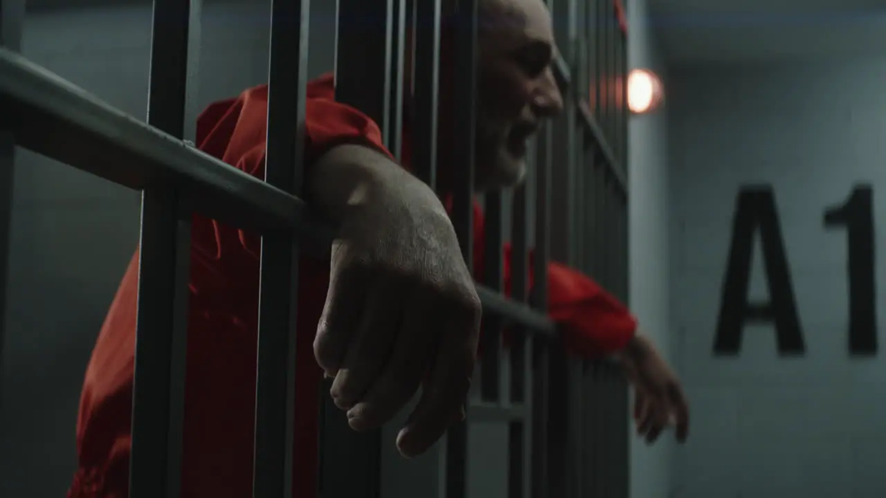 Elderly Prisoner in Orange Uniform Cries Holds His Hands on Metal Bars