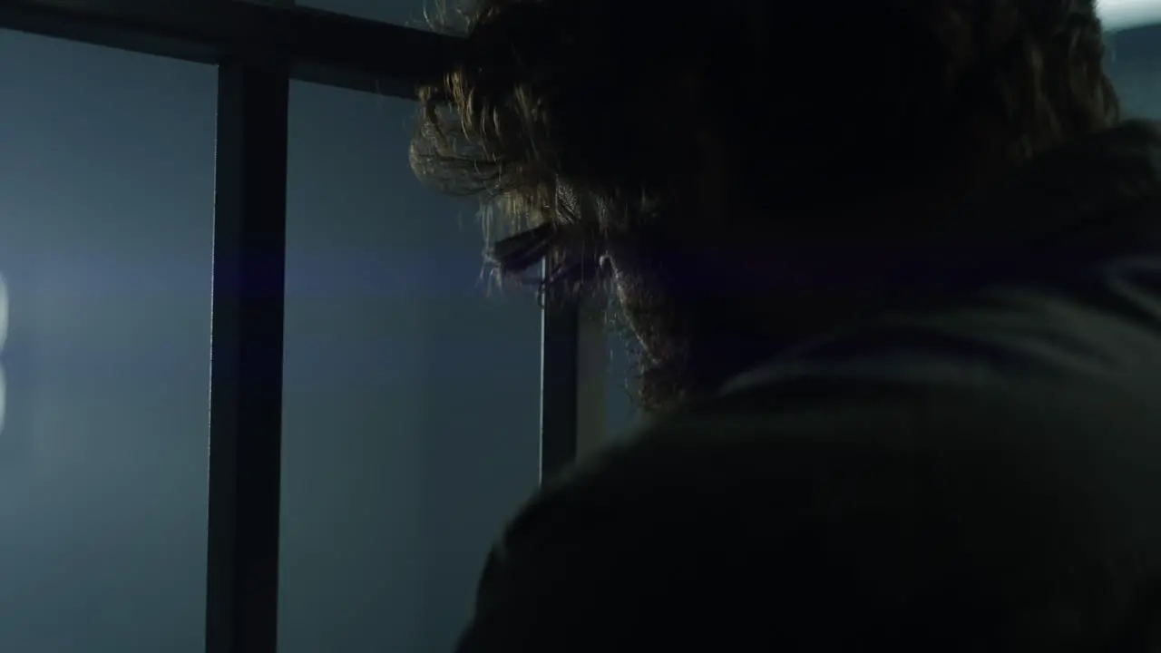 Male Criminal Stands Facing the Metal Bars in Prison Cell