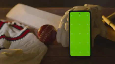 Green Screen Mobile Phone Surrounded By Cricket Bat Ball And Clothing On Wooden Surface 1