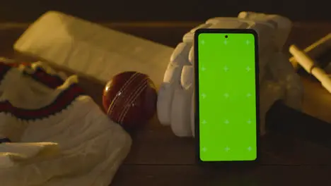 Green Screen Mobile Phone Surrounded By Cricket Bat Ball And Clothing On Wooden Surface 3