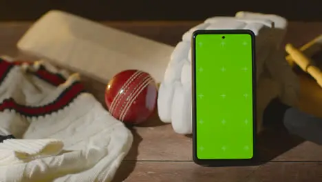 Green Screen Mobile Phone Surrounded By Cricket Bat Ball And Clothing On Wooden Surface