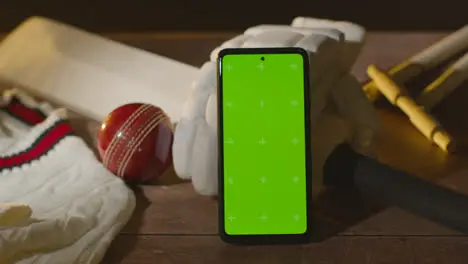 Green Screen Mobile Phone Surrounded By Cricket Bat Ball And Clothing On Wooden Surface 2