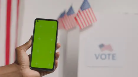 Close Up Of Hand Holding Green Screen Mobile Phone In Front Of Ballot Box In American Election 1