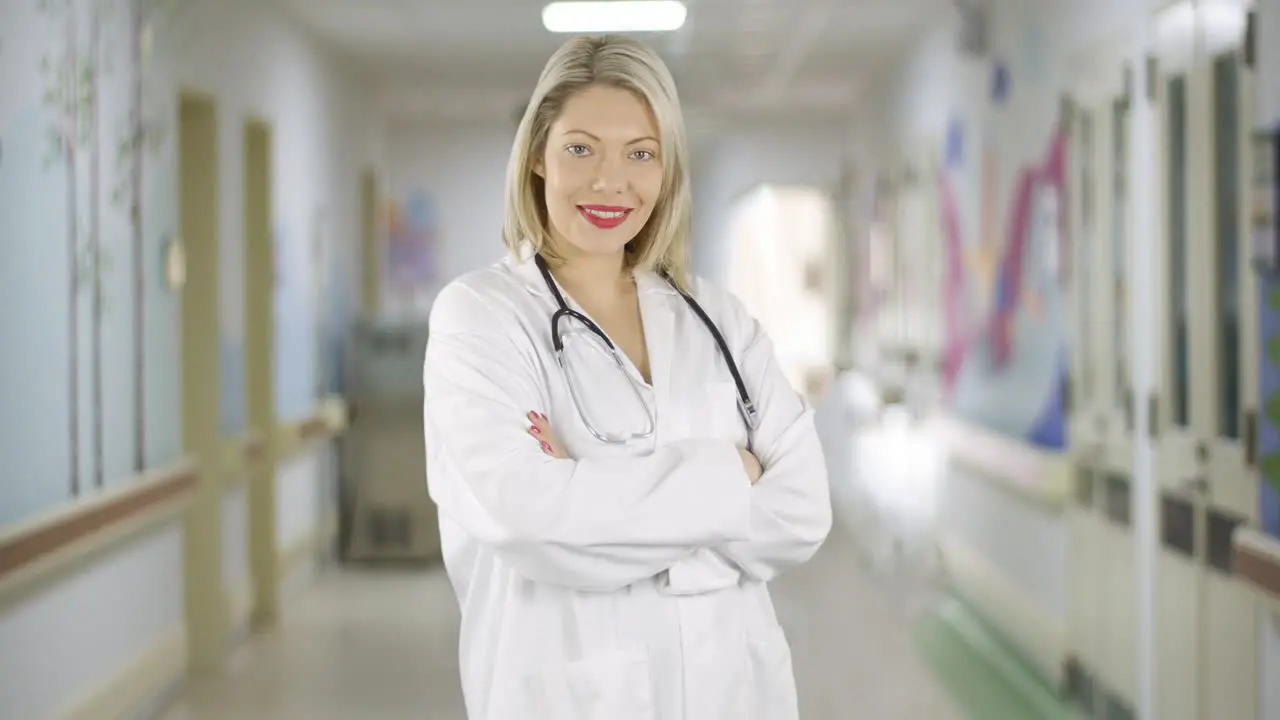 Happy attractive blonde haired female doctor turns and smiles in a hospital corridor