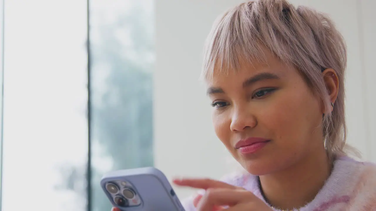 Close Up Of Young Woman At Home Scrolling Through Social Media On Mobile Phone