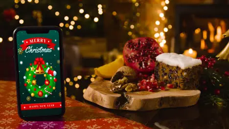 Mobile Phone With Merry Christmas Message With Festive Food Tree And Presents In Background