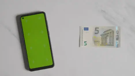 Overhead Currency Shot Of Hand Grabbing 5 Euro Note Next To Green Screen Mobile Phone