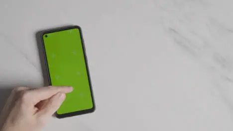 Overhead Shot Of Person Using Green Screen Mobile Phone On Marble Surface