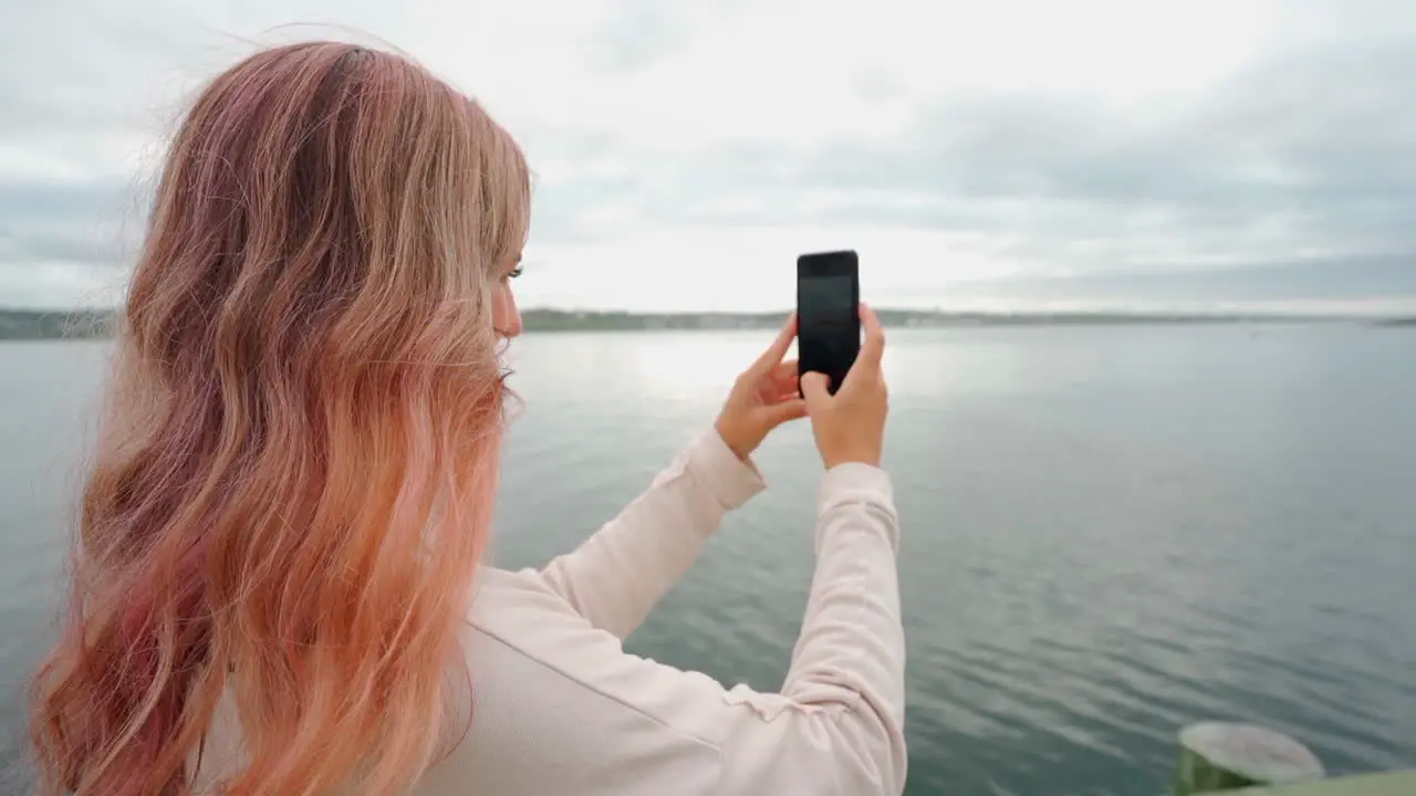 Smiling woman with pink hair on the coast of eastern Canada taking a phone on her cell phone during midday