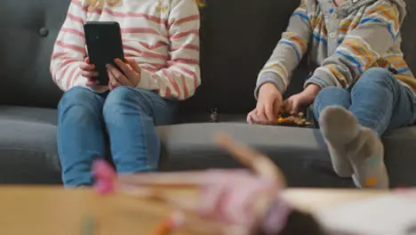 Close Up Of Boy Playing With Toy Dinosaurs As Girl Uses Mobile Phone