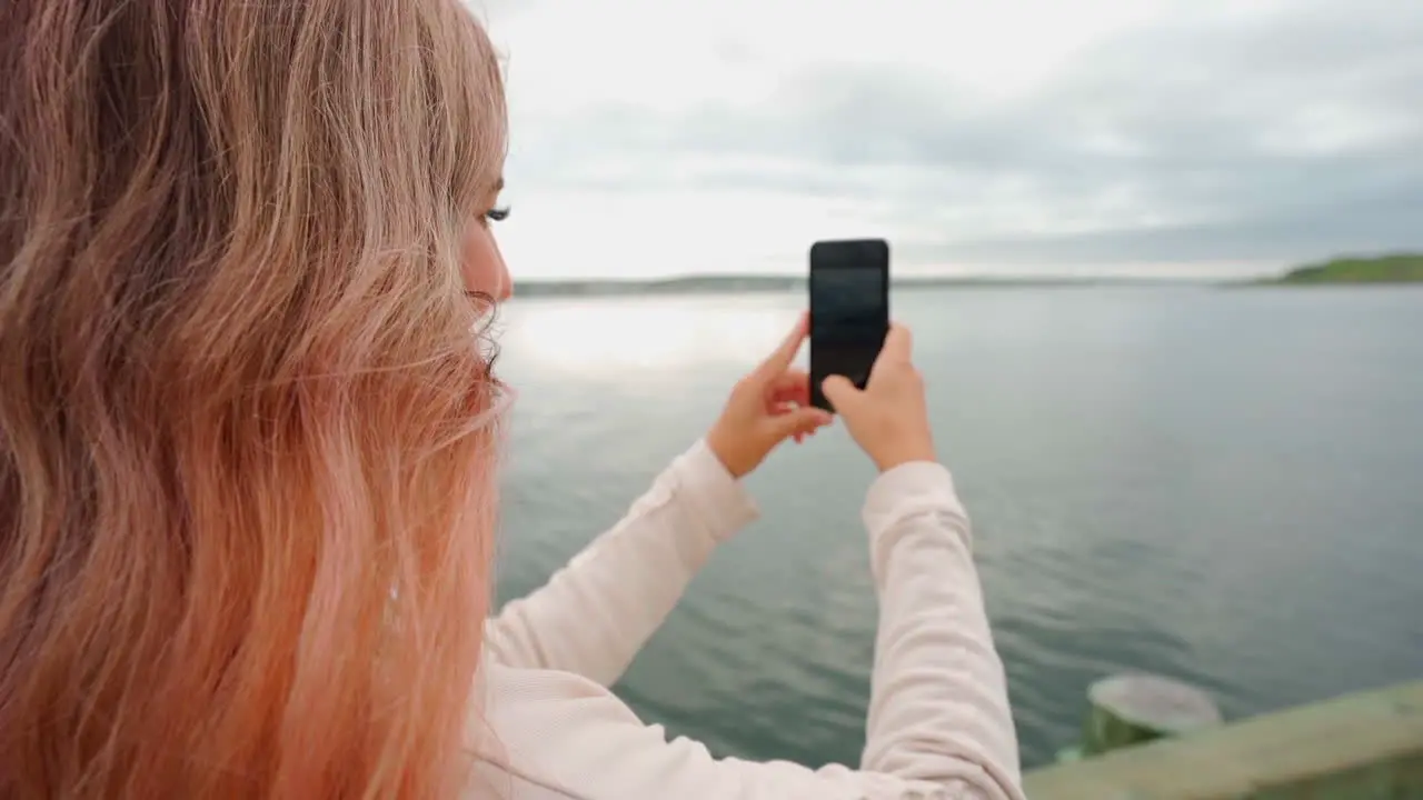 Woman with pink hair on the coast of eastern Canada taking a photo on heriphone during midday