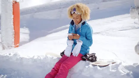 Woman sitting on snowbank texting