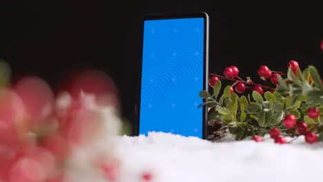 Blue Screen Mobile Phone On Christmas Background With Snow And Foliage