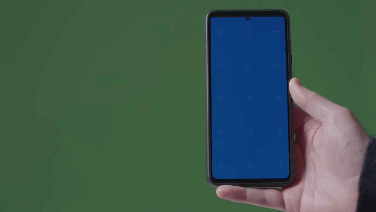 Close Up Of Person Holding Blue Screen Mobile Phone Against Green Background 1