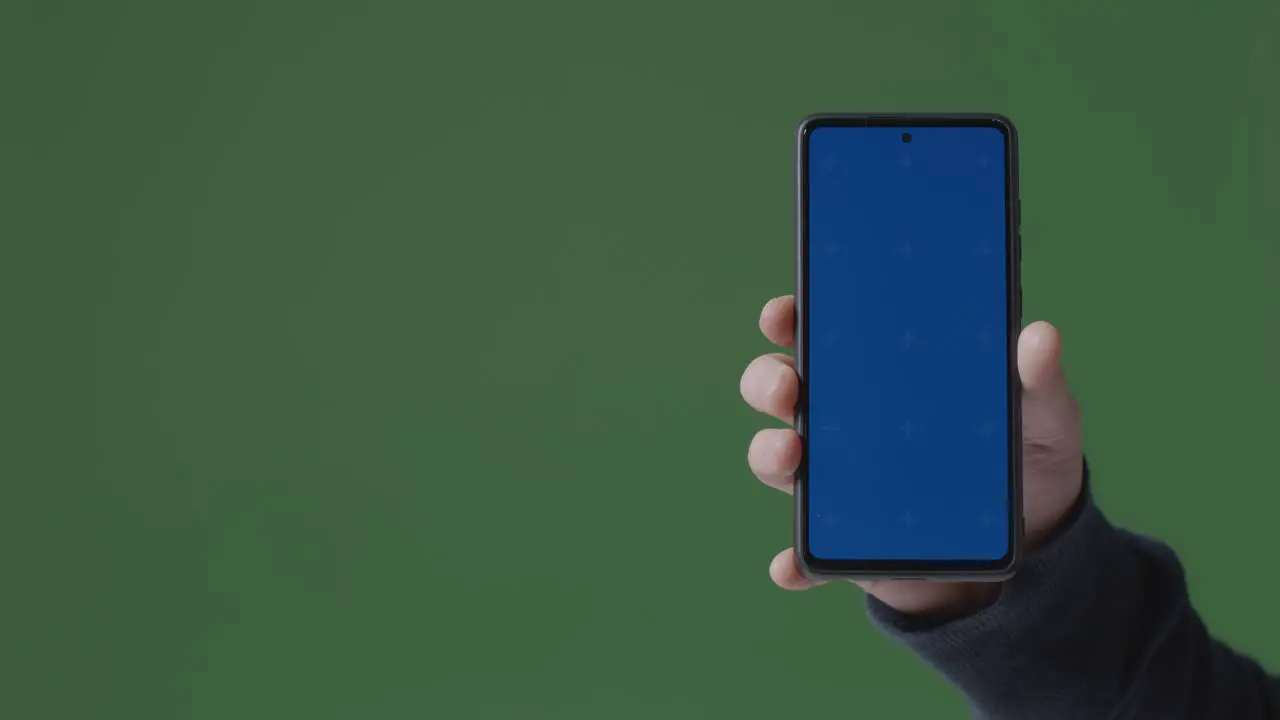 Close Up Of Person Holding Blue Screen Mobile Phone Against Green Background