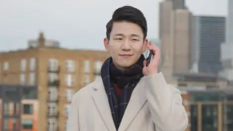 Young Asian Businessman Talking On Mobile Phone With London City Skyline In Background 2