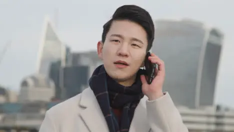 Young Asian Businessman Talking On Mobile Phone With London City Skyline In Background