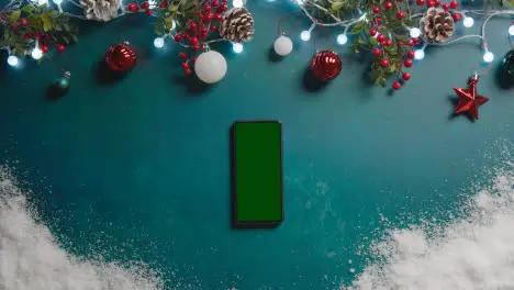 Overhead Shot Of Green Screen Mobile Phone With Christmas Decorations And Snow