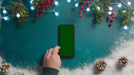 Overhead Christmas Background With Green Screen Mobile Phone Snow Lights Holly And Pine Cones