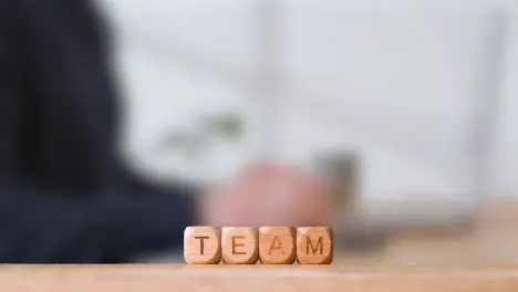 Business Concept Wooden Letter Cubes Or Dice Spelling Team With Office Person Using Mobile Phone In Background