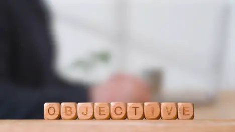 Business Concept Wooden Letter Cubes Or Dice Spelling Objective With Office Person Using Mobile Phone In Background