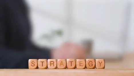 Business Concept Wooden Letter Cubes Or Dice Spelling Strategy With Office Person Using Mobile Phone In Background