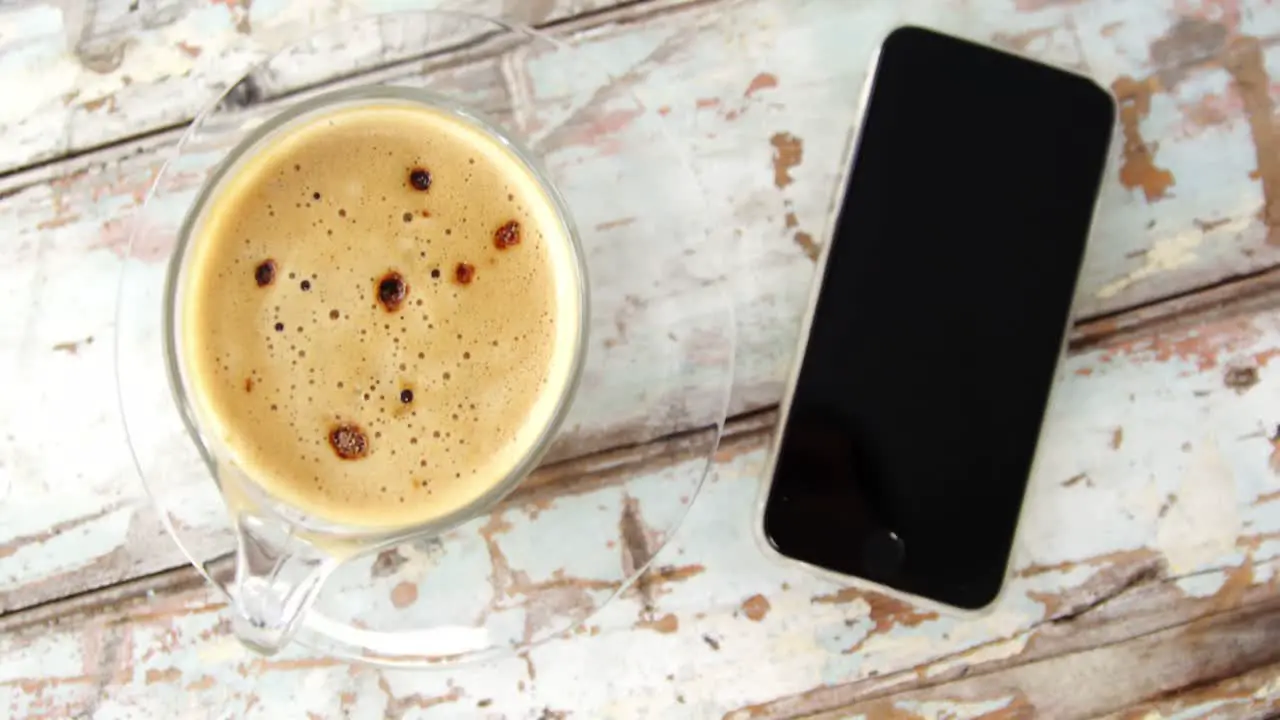 Coffee cup and mobile phone on wooden plank