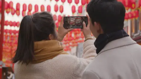 Asian Couple On Holiday Taking Photo In Chinatown In London UK On Mobile Phone