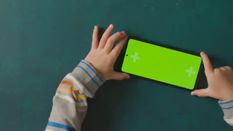 Overhead Studio Shot Of Child Scrolling On Green Screen Mobile Phone 1