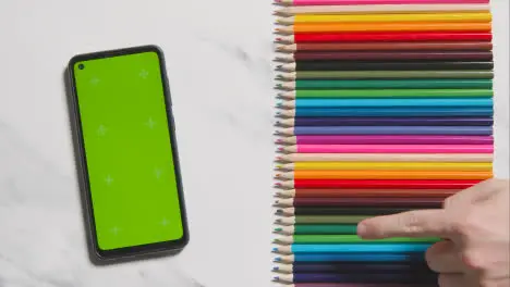 Coloured Pencils In A Line On Marble Background With Person Choosing Red One And Green Screen Mobile Phone