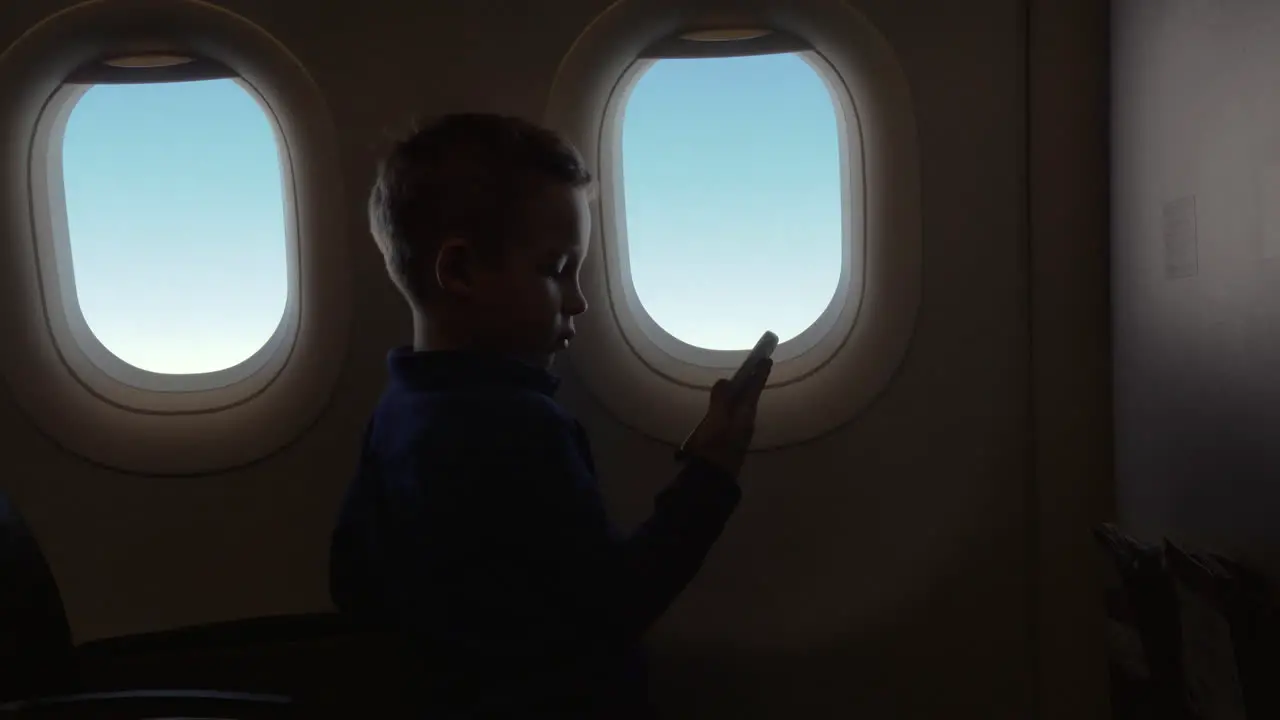 In cabin of plane little boy holding a phone and watching a video