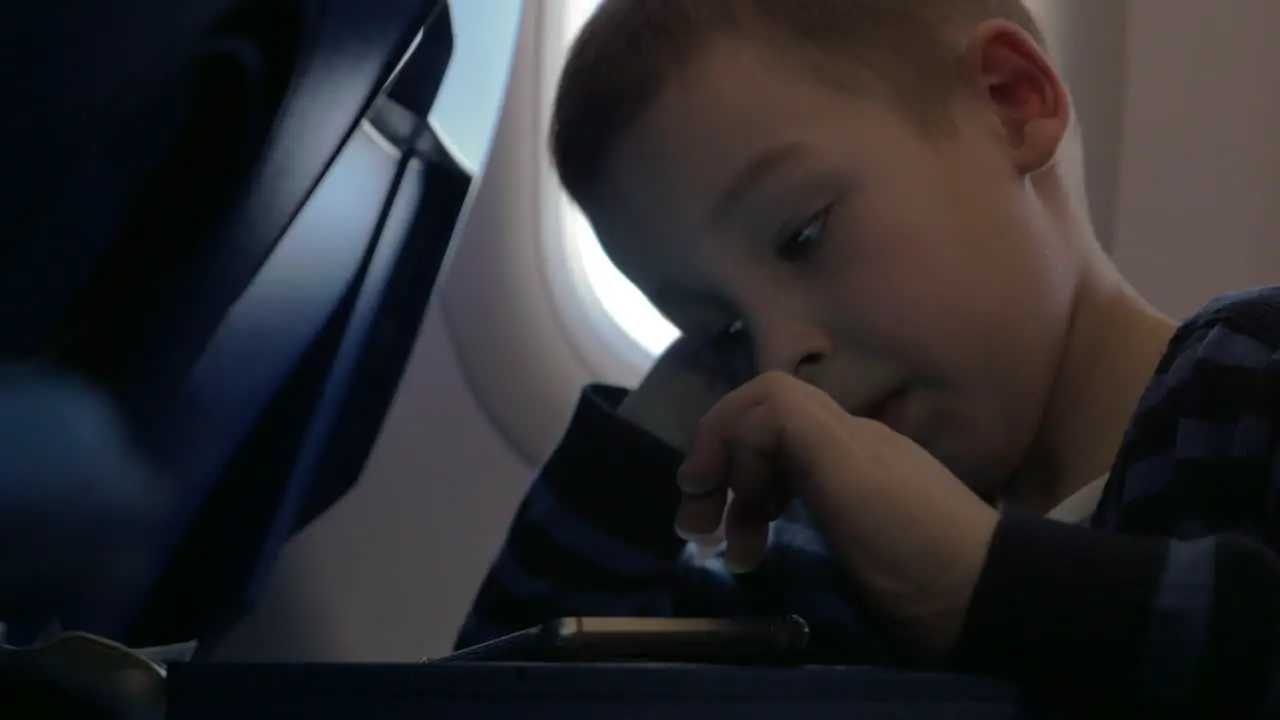 In plane sits a little boy and playing games on the mobile phone