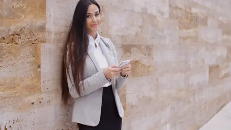 Business woman leaning against wall texting