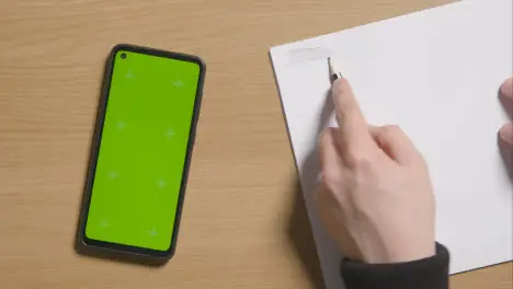 Person Sketching With Pencil On Pad On Wooden Table Background Next To Green Screen Mobile Phone 