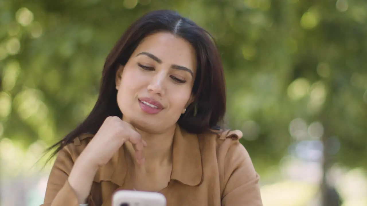 Muslim Woman Sitting At Outdoor Table On City Street Sending Text Message To Date On Mobile Phone