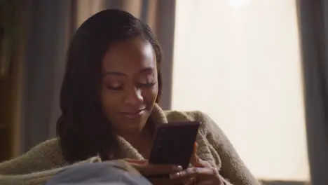 Close Up Of Young Woman Relaxing At Home Sitting On Sofa Scrolling Through Mobile Phone