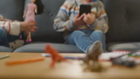 Close Up Of Girl Playing With Toy Doll As Boy Uses Mobile Phone