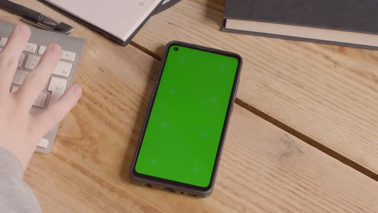 Close Up Of Green Screen Mobile Phone On Desk With Hand Typing On Computer Keyboard 2