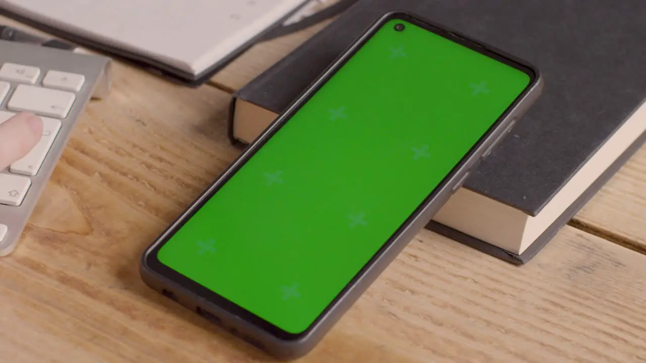 Close Up Of Green Screen Mobile Phone On Desk With Hand Typing On Computer Keyboard