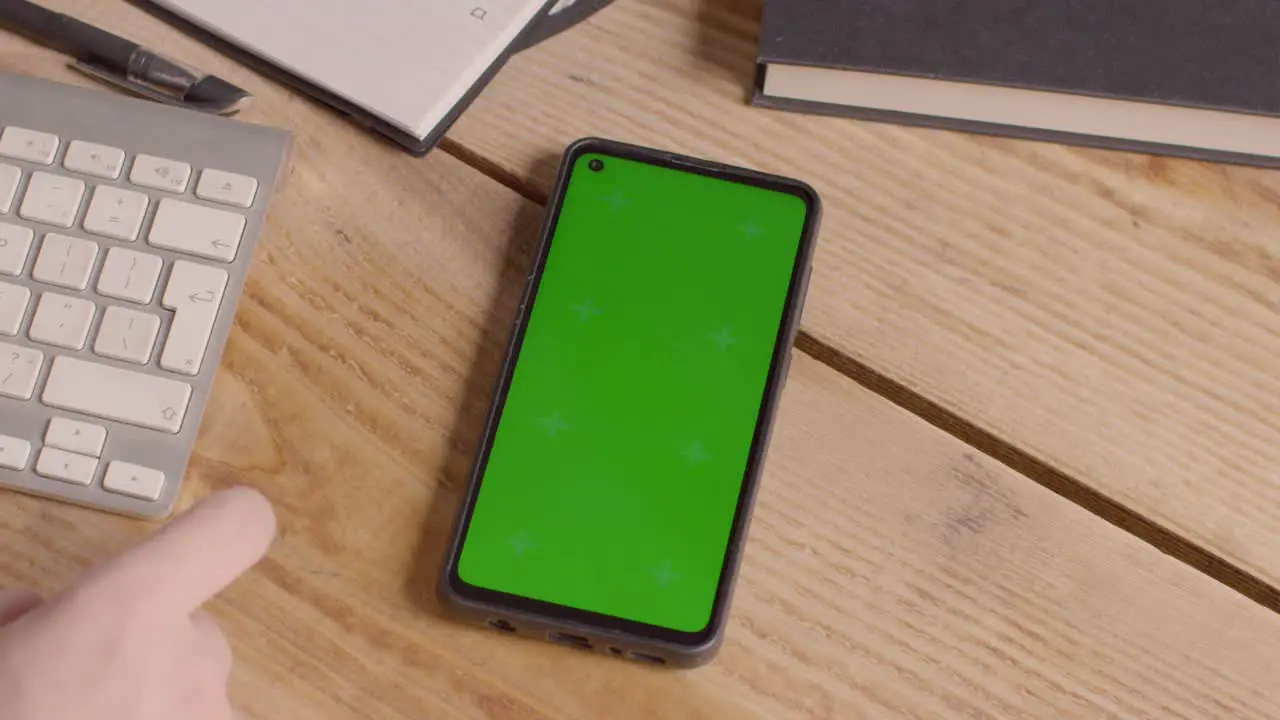 Close Up Of Green Screen Mobile Phone On Desk With Hand Scrolling Across Screen