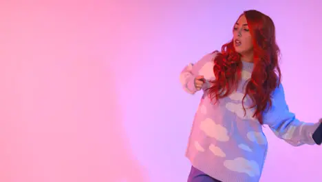 Studio Shot Of Young Gen Z Woman Dancing Against Pink Background Holding Mobile Phone