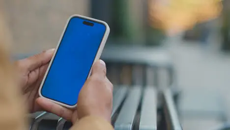 Close Up Of Muslim Man Sitting Outdoors On City Street Looking At Blue Screen Mobile Phone