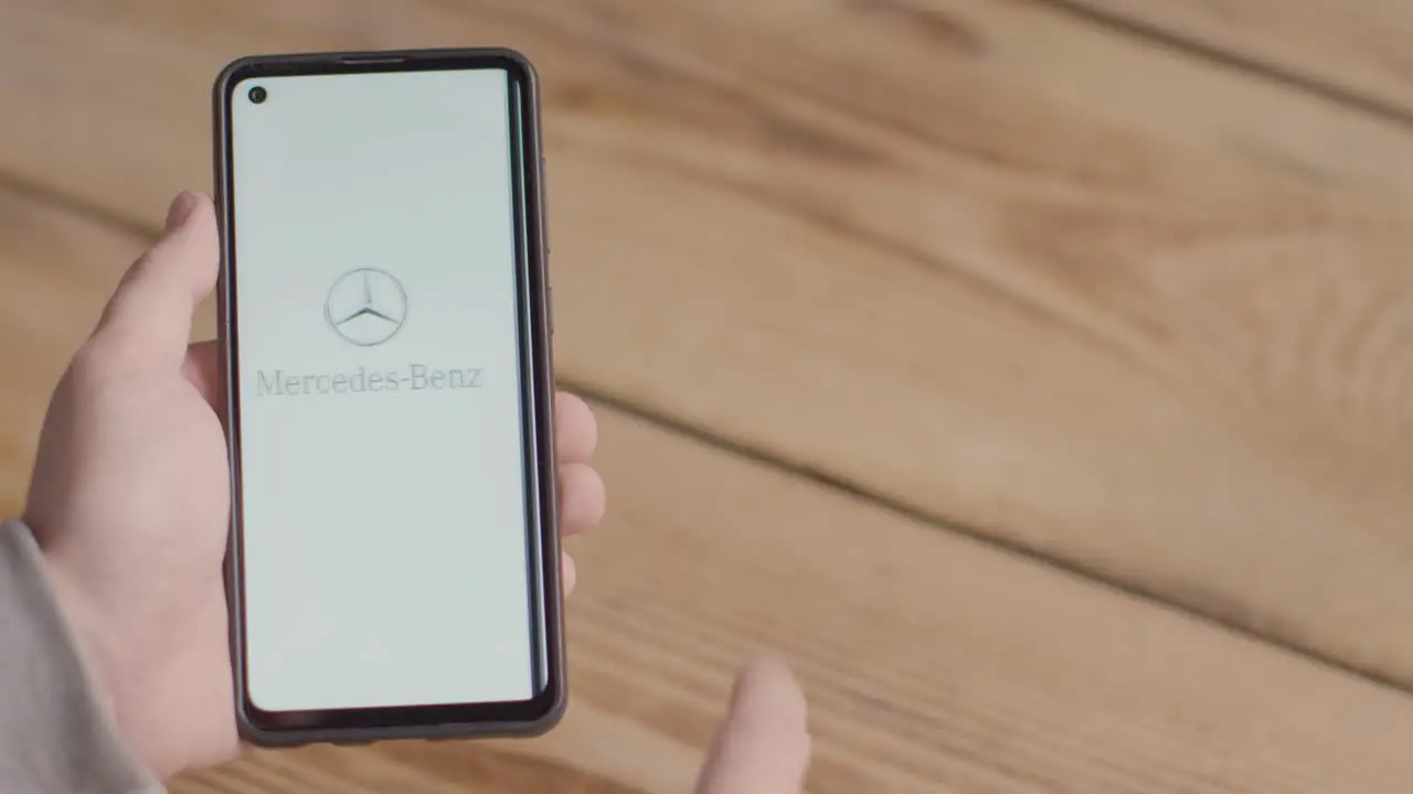 Hand Holding Mobile Phone With Screen Showing Brand Logos For Tesla Mercedes Benz BMW and Toyota