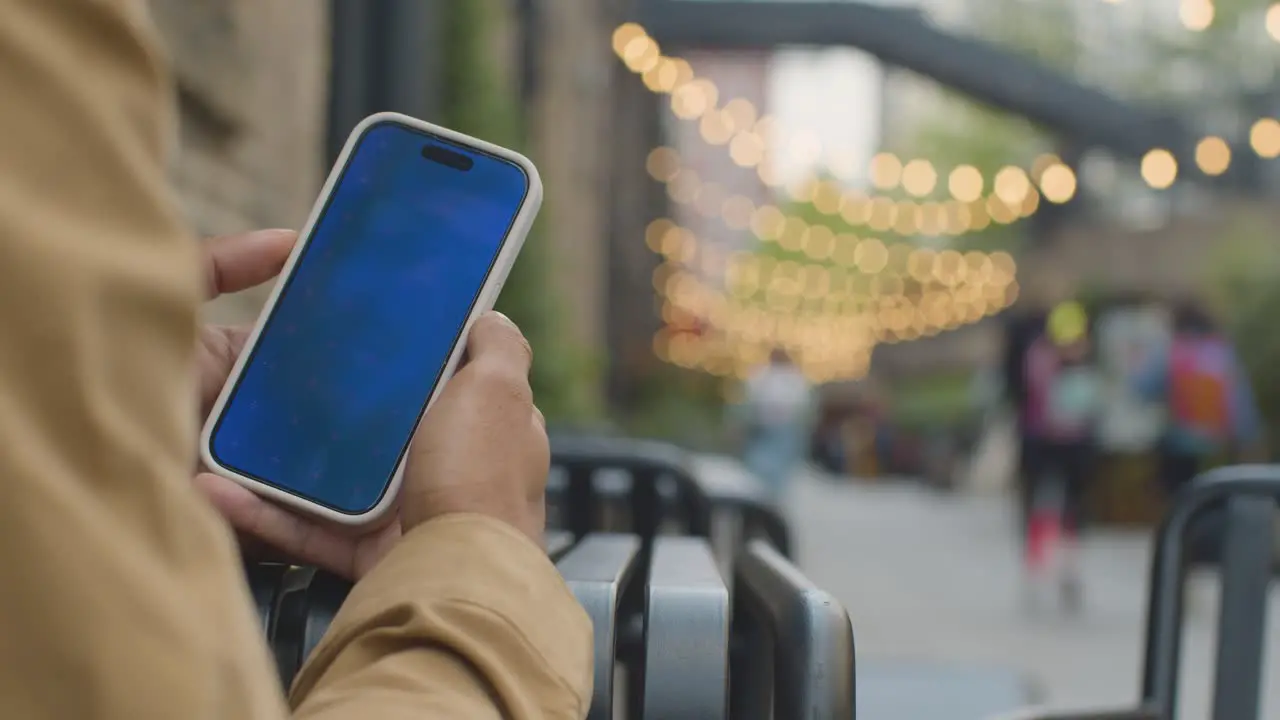 Close Up Of Muslim Man Sitting Outdoors On City Street Looking At Blue Screen Mobile Phone 1