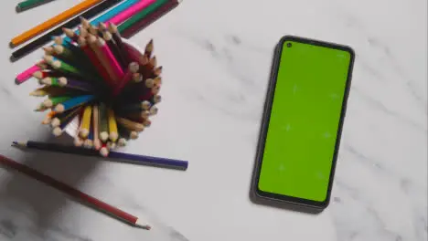 Overhead Shot Of Multi-Coloured Pencils In Pot And Green Screen Phone On Marble Background