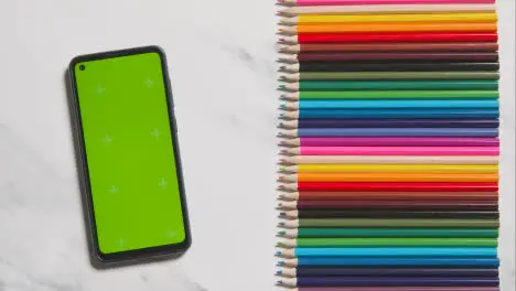 Coloured Pencils In A Line On Marble Background With Person Scrolling Through Green Screen Mobile Phone